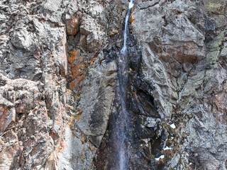Extreme close-up of a narrow stream of water cascading down a highly textured rock face with...