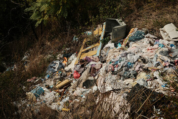Pile of plastic waste and discarded clothes on illegal dump site in mountain area symbolizing pollution and environmental problem