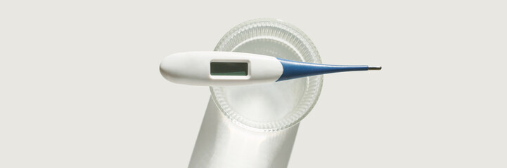 Digital thermometer in glass cup on light background for temperature measurement and health...
