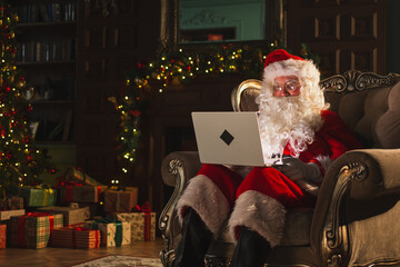 Merry Christmas. Santa Claus with laptop reading letters from children typing buying presents gifts...
