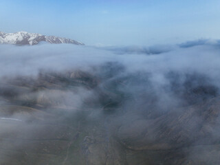 Aerial shot of low-hanging clouds completely obscuring a deep mountain valley, with only the dark outlines of the surrounding peaks visible at twilight