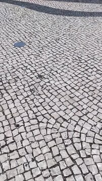 Traditional paving in a pedestrian area in Lisbon, Portugal, composed of small pieces of stone, usually basalt (black) and limestone (white), arranged to form patterns or images, similar to a mosaic.
