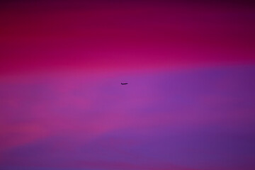 A winter sky glows with deep blues and soft pinks, merging into violet, as a tiny commercial airplane crosses the horizon.