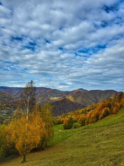 Beautiful landscape view of mountains in the fall with colorful forest trees, green pasture and blue sky with white clouds. Muntele Rece, Cluj, Romania
