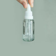 Transparent serum bottle held in hand against soft green background.