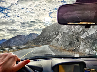 Scenic drive along winding mountain road with dramatic sky and rocky terrain