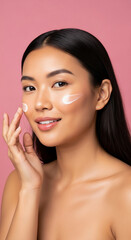 Asian woman applying skincare cream to her face with a gentle smile.