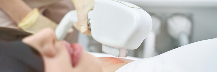 Naklejka premium Caucasian female undergoing laser hair removal treatment in clinic, close-up view of equipment and patient.