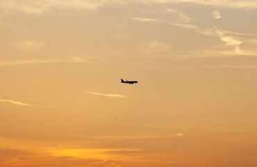 Airplane flying at sunset with orange sky and clouds
