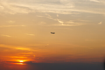 Airplane flying at sunset in cloudy sky