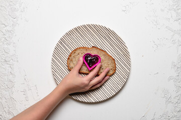 Hand Holding a Heart-Shaped Mold with Jam on Bread Slice