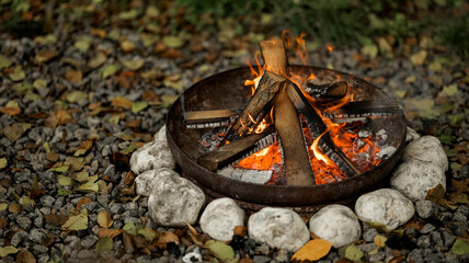 Cozy campfire burning in a stone fire pit with autumn leaves around