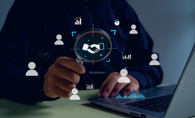 Business partnership and digital collaboration concept. A businessman using a magnifying glass with handshake and data analytics icons, representing trust, teamwork, and corporate relationship.