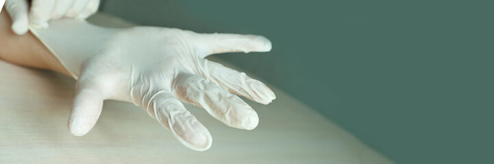 Close-up of a hand wearing a latex glove against a green background.