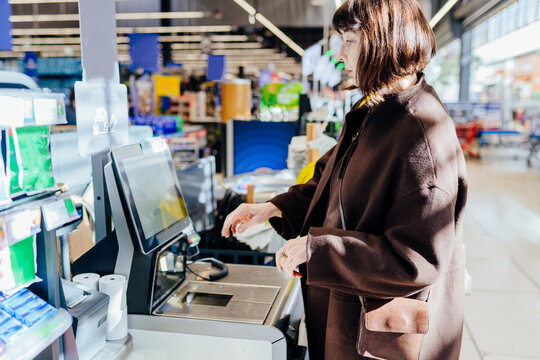 Senior woman using self checkout terminal at supermarket with reusable tote bag - Powered by Adobe
