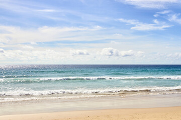 Peaceful sandy beach with clear blue sky and gentle ocean waves on a sunny day.