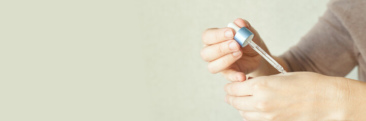 Close-up of hands applying serum with dropper on skin for skincare routine and hydration.