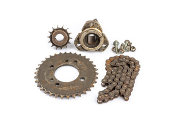 A close-up of a dirty, oily, and greasy chain, sprockets, and wheel hub on an old motorcycle against a white background. The image captures the essence of repair and maintenance.