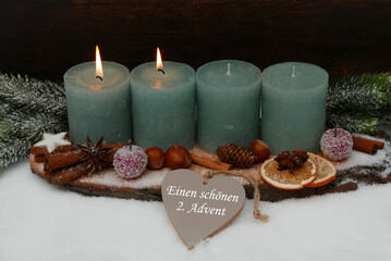 Zweiter Advent: Natürliche Adventsdekoration mit grünen Kerzen, Tannenzweigen,Zimtstangen und Nüssen auf einer Baumscheibe arrangiert.