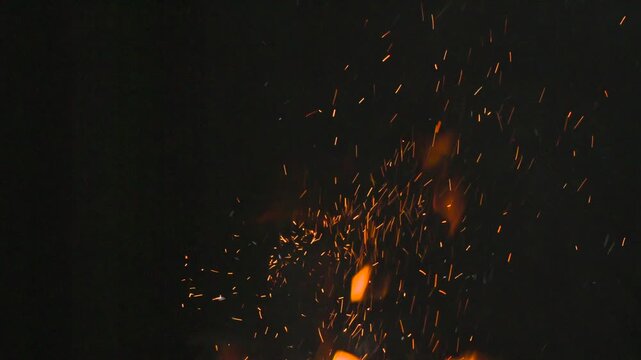 Sparks from a Fire in the Night Sky. Tongues of flame and red-hot sparks slowly soar up in the dark. Filmed at a speed of 120fps