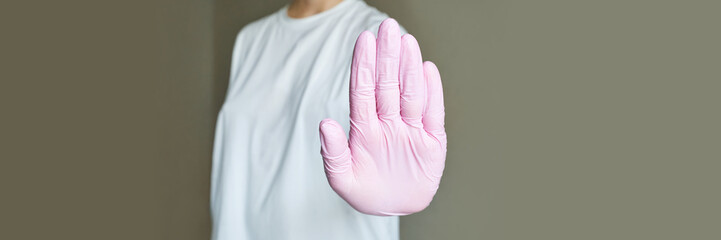 Caucasian female adult with raised hand wearing pink gloves and white t-shirt demonstrating stop...