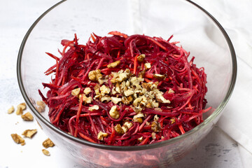 Healthy beetroot salad with shredded carrot, celery, onion, and chopped walnuts in a glass bowl on light textured background. Fresh vegetarian dish, close-up, with copy space for text or design