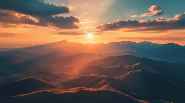 Aerial view of mountain range at sunset with sun rays shining through clouds