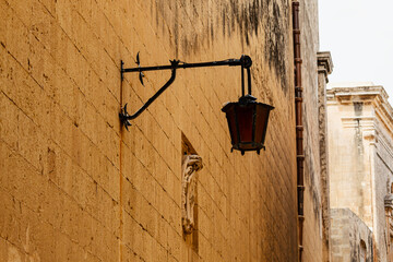 A vintage black metal lantern is mounted on a textured, light brown stone wall in an old city...
