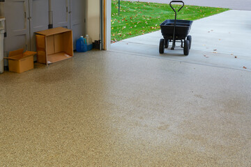 An epoxy covered garage floor with a black garden wagon cart in the open doorway near the green lawn.