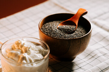 Roasted chia seeds in a wooden bowl beside a creamy dip on a checkered tablecloth