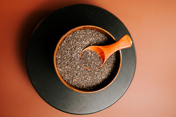 Roasted chia seeds in a wooden bowl with a spoon on a dark surface