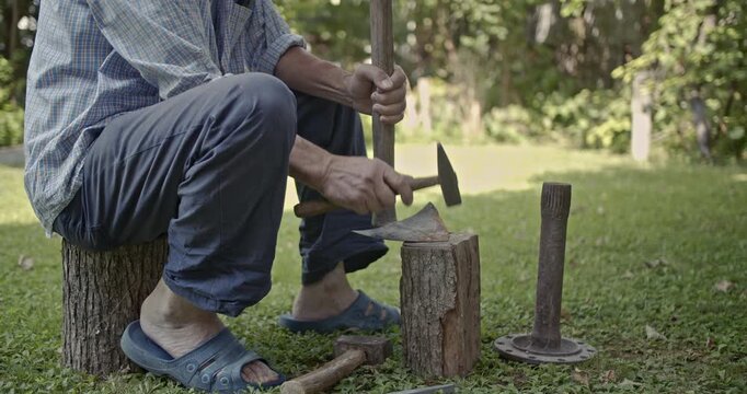 A close-up shot captures a man diligently sharpening an old axe using a hammer on a tree stump, with audible sounds of the work. This video emphasizes traditional tools and manual labor.