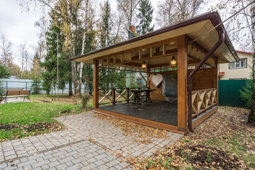 Fototapeta premium Wooden gazebo in quiet garden surrounded by trees and autumn leaves, perfect for relaxation and gatherings