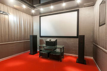 A stylish home theater features a large screen, sound speakers, and a sleek table. The room has soft lighting and a red carpet