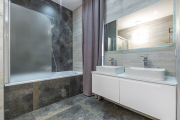 A sleek bathroom features dual sinks, a modern shower with a frosted door, and elegant tiled walls....