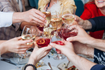 Group of guests celebrate and raise glasses, toasting and cheering with alcohol glasses with wine and champagne in the restaurant on corporate christmas birthday party event or wedding celebration