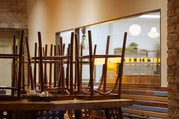 Chairs are stacked upside down on wooden tables in a restaurant after closing time. The kitchen is...