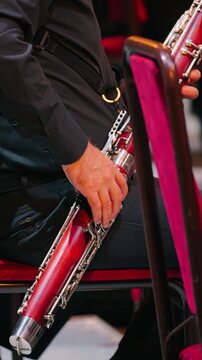 A close-up of a musician playing the bassoon. He is dressed in a black suit. His fingers are pressing the keys of the instrument