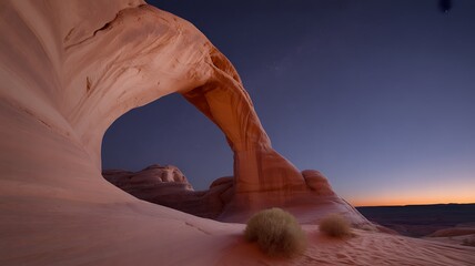 Natural sandstone arch glows in soft light at twilight with a deep blue sky above