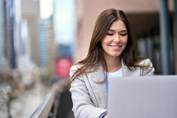 Happy young business woman worker or student working on laptop computer outdoors in outdoor cafe. Professional businesswoman employee sitting at cafe table relaxing browsing internet online.