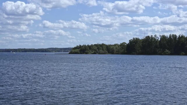 A Wide Blue Lake Stretches To A Tree-lined Shore And Distant Town Under A Big Dynamic Sky Filled With White Clouds