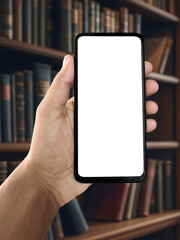Hand holding smartphone with library in background, shelves full of books and warm reading light, education and knowledge concept, digital learning or study app idea, modern technology in academic spa