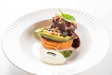 A gourmet dish featuring seared beef tenderloin on a crispy potato pancake, topped with a roasted pepper, fresh spinach leaves, fried onions, and a rich sauce, served with a side of cream