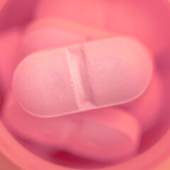 Single, pink, oblong pill, selective focus, close-up, abstract, pharmacologic background.