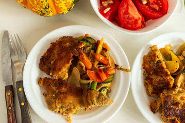 Crispy fried fish fillets served with roasted carrots, zucchini, and fresh tomato salad. A rustic homemade meal that highlights traditional cooking and healthy eating.