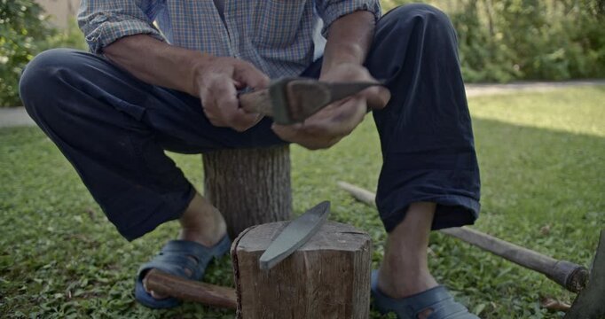 Watch an experienced man meticulously sharpening an axe outdoors using a traditional whetstone. This detailed 4K video includes the crisp, authentic sounds of the metal being honed.