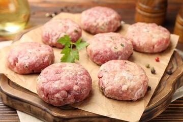 Raw meat patties with parsley and peppercorns on wooden table, closeup