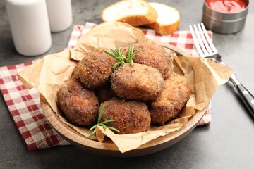 Delicious patties with rosemary in bowl on grey textured table, closeup