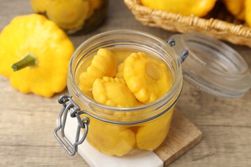 Pickled pattypan squashes in glass jar and fresh vegetables on wooden table, closeup