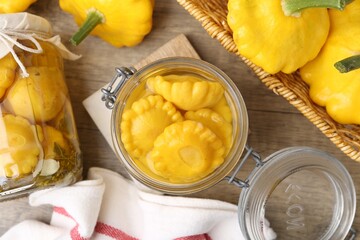 Pickled pattypan squashes in glass jars and fresh vegetables on wooden table, flat lay
